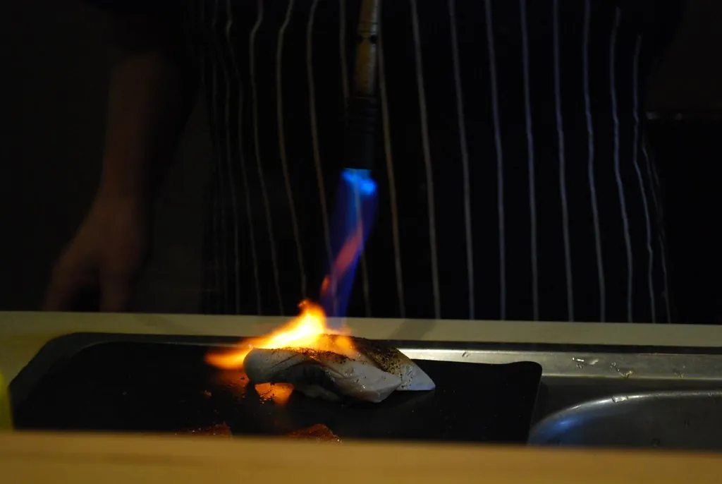 Llama de soplete sobre una pieza de nigiri en la barra