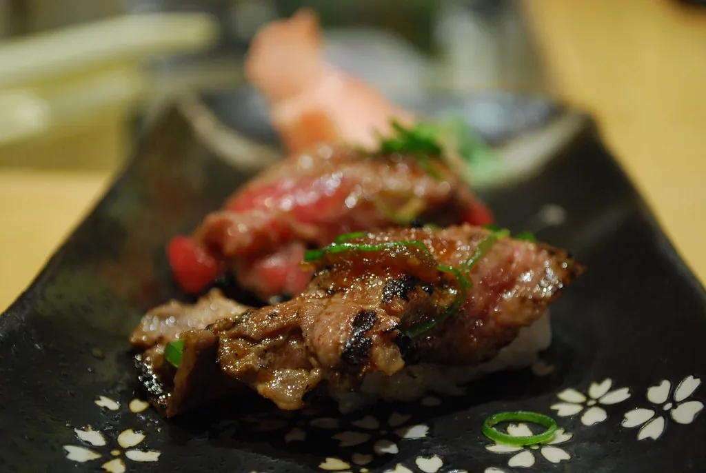 Nigiri de wagyu braseado sobre plato negro con flores blancas