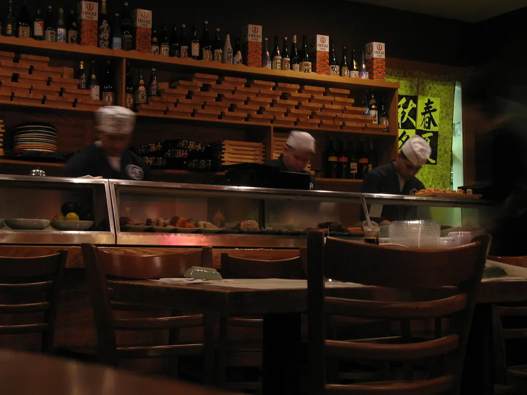 Barra de sushi en penumbra con dos cocineros trabajando